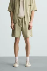 Bermuda de algodón color blanco, de corte relajado (relaxed fit), con cintura elástica ajustable mediante cordón. Posee bolsillos laterales y un bolsillo trasero de plastrón. Presenta un bordado en contraste en la pernera.