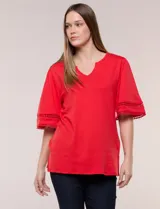 Remera blanca de silueta recta y algodón suave, con escote redondo y pequeña abertura central tipo gota. Presenta mangas de largo intermedio con aplicación horizontal de puntilla calada al tono y ruedo recto con tajos laterales.