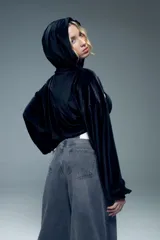 Canguro corto negro de terciopelo con capucha, mangas largas abullonadas con puños elastizados y abertura en el pecho.