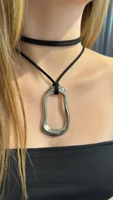Gargantilla doble compuesta por un choker de gamuza negra y un collar largo con dije metálico de forma irregular y orgánica en tono plateado.