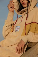 Hoodie de tela de toalla color azul, con cuello alto y cierre frontal de cremallera amarilla. Presenta bloques de color rojo en los hombros y detalles de ribetes amarillos. Tiene un bolsillo tipo canguro y un parche decorativo en el pecho.