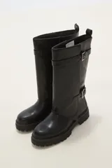 Bota de caña media en color negro, confeccionada en eco cuero con suela track dentada. Presenta un diseño con doble tira ajustable con hebillas metálicas en el lateral externo.