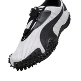 Championes Puma modelo Mostro Perforated, de diseño bajo con exterior de cuero perforado en color blanco y detalles en negro. Presenta una suela distintiva con relieve de tachones y cierre de velcro en el empeine.