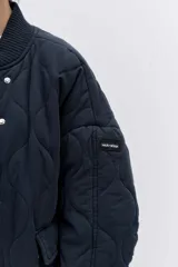 Cazadora tipo bomber de color negro con diseño acolchado de rombos, cuello, puños y ruedo acanalados, cierre frontal y bolsillos laterales.