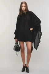 Camisa negra de crepé liviano y translúcido, de calce regular, diseño asimétrico con volados en el lado izquierdo, mangas largas con puños elásticos y volados, cuello redondo y cierre frontal con cartera oculta y botones metálicos.