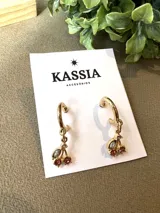 Aros dorados tipo argolla con dije de cerezas rojas y hojas blancas.