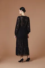 Vestido largo color crudo de encaje, con mangas largas abullonadas, cuello redondo y falda con paneles traslúcidos.