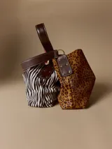 Cartera tipo hobo de cuero azul con textura granulada. Presenta un diseño holgado, con una correa de hombro bicolor que combina azul y rojo, sujeta por argollas metálicas. Incluye una placa metálica pequeña con el logo de la marca en la parte inferior frontal.