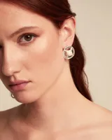 Par de aros plateados con forma circular y diseño calado con perla blanca en el centro.
