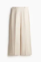 Pantalón sastrero de tiro alto en color beige, con perneras amplias y raya marcada en la parte delantera y trasera. Cuenta con cierre de cremallera, botón oculto y corchete, además de bolsillos decorativos insertados.