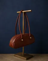 Cartera estilo baguette de cuero, con diseño estructurado y silueta alargada. Presenta manijas largas con detalles de nudos esféricos metálicos en la unión.
