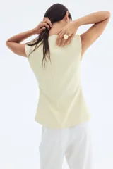 Chaleco de punto interlock color crema, entallado, con escote en V pronunciado y manga japonesa. Presenta una hilera de botones metálicos pequeños en el frente que generan un ligero corte acampanado en la parte inferior.