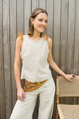 Chaleco de punto color beige con cuello redondo y detalle de plumas en los hombros. Presenta un diseño de espalda irregular y corte al cuerpo.