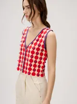 Top de punto sin mangas con escote en V, cierre frontal con botones y estampa geométrica de círculos rojos sobre fondo beige, con detalles en color violeta y apliques en relieve.