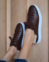 Zapatilla urbana de cuero marrón con cordones al tono y suela de plataforma blanca. Presenta un detalle de refuerzo en el talón en color beige.