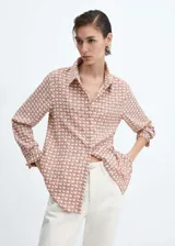 Camisa de corte recto y tejido fluido, con cuello camisero clásico, cierre frontal de botones y mangas largas con puños abotonados.