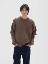 Buzo de punto color marrón, con cuello redondo, mangas largas y puños acanalados. Presenta un pequeño bordado con la palabra 'PASTICHE' en el pecho.