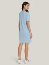Vestido Tommy Hilfiger celeste de corte recto, con cuello redondo y mangas cortas. Presenta un logo script de la marca estampado en el pecho y la bandera de Tommy Hilfiger bordada en la manga.