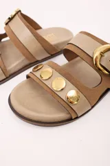 Sandalias bajas de cuero marrón con doble tira, hebilla ajustable y apliques de tachas metálicas.