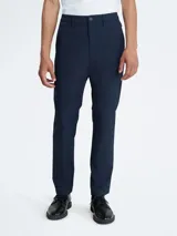 Pantalón chino de hombre, color azul marino, de corte slim y tiro medio. Presenta cierre frontal con botón y cremallera, trabillas para cinturón y bolsillos laterales y traseros.