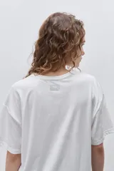 Remera blanca de calce relajado y silueta amplia, con cuello redondo, mangas cortas y estampa gráfica frontal de un cangrejo sobre franjas en tonos rosado y rojo.