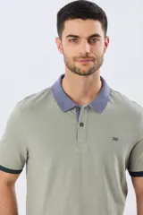 Remera polo de manga corta en color verde militar, con cuello y detalles en las mangas de color gris y azul oscuro. Cuenta con cierre frontal de botones y pequeño bordado en el pecho.