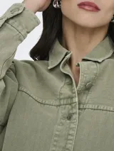 Sobrecamisa de jean de color negro gastado, con cuello camisero, cierre frontal de botones metálicos, bolsillos frontales de parche y mangas largas.