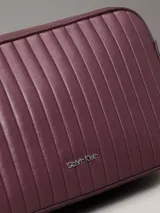 Cartera bandolera Calvin Klein color borgoña con diseño acolchado vertical. Tiene correa de cadena plateada, cierre superior con cremallera y logo metálico en el frente.