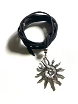Collar con dije de sol en espiral de acero quirúrgico y lazo de cuero negro con detalles metálicos.