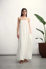 Vestido largo color beige, de corte recto y textura arrugada. Tiene tirantes finos con detalle de cordón marrón.
