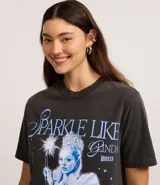 Remera de algodón color gris oscuro (efecto desteñido/vintage) con estampa frontal inspirada en el personaje Glinda, el Hada Buena, de la película Wicked. La estampa incluye el texto "SPARKLE LIKE GLINDA WICKED" y una ilustración de Glinda con su varita mágica.