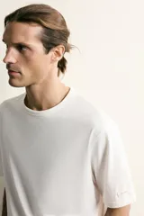 Camiseta relaxed fit color blanco, de cuello redondo y manga corta. Presenta un pequeño parche aplicado a contraste en el extremo de la manga y terminaciones en rib.