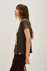 Remera de algodón color marrón oscuro con cuello redondo y manga corta. Estampado frontal con flores blancas y detalles en lentejuelas doradas, hojas verdes y texto en azul oscuro que dice "TRÈS CHIC".