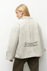 Tapado corto color beige de tejido grueso con cuello alto, cierre frontal con botones grandes veteados y bolsillos delanteros.