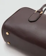 Bolso de mano de poliuretano color marrón oscuro, con diseño rectangular estructurado, cierre de solapa frontal y asa corta de hombro.