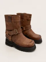Bota de punta cuadrada realizada en cuero encerado color marrón, con hebillas en la caña, herrajes de níquel y fondo de suela negro.