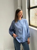 Camisa azul de lino con cuello mao, cierre frontal con botones y mangas largas abullonadas con puños elásticos.