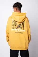 Buzo canguro amarillo ocre oversize de algodón rústico con capucha, cordones negros con letras blancas, bolsillo frontal y puños y cintura acanalados. Presenta estampados en el frente y las mangas.