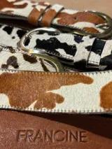 Cinto de cuero vacuno con pelo natural, con diseño de manchas tipo animal print. Cuenta con hebilla metálica y costuras reforzadas.
