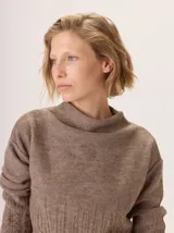 Buzo de lana color beige claro, con cuello chimenea y manga larga. Presenta trenzas de punto grueso en el frente y en los puños, con un diseño texturizado que se asemeja a espigas o ramas.