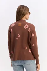 Sweater de tejido de punto color marrón con diseño estampado de flores en tonos rosados. Presenta cuello alto, mangas largas con puños ajustados y un corte relajado con terminación recta en la cintura.