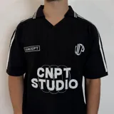 Chomba de tejido de punto color negro, con cuello polo y cierre frontal parcial. Presenta diseño de rayas verticales sutiles en el tejido, detalles de líneas blancas en los hombros y estampado frontal con texto y gráficos en color blanco.