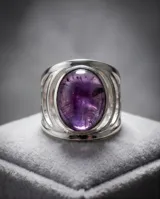 Anillo de plata con piedra natural de amatista en corte ovalado, diseño ancho con detalles geométricos en los laterales.
