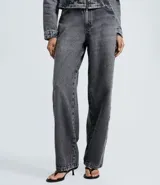 Pantalón baggy de jean color gris desteñido, con corte amplio y recto. Presenta una hilera de ojales metálicos decorativos a lo largo de los laterales y cierre frontal con botón y cremallera.
