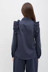 Camisa de gabardina de tencel color negro, con cuello clásico, cierre frontal de botones y volados fruncidos en los hombros.