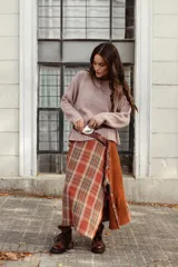 Falda midi de corte irregular, confeccionada en una combinación de tela escocesa en tonos rojizos y tela afieltrada color terracota. Presenta un diseño con tajos laterales y tiro a la cintura.