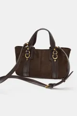 Bolso de mano tipo mini shopper en color marrón oscuro, confeccionado en material tipo gamuza o nobuk, con detalles de cuero liso en las asas y tiras laterales. Presenta herrajes metálicos dorados con forma de doble 'C' o anillo.