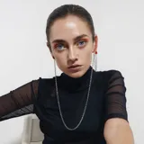 Aro trepador asimétrico de acero quirúrgico plateado, con un círculo rojo en la parte superior y cadenas colgantes.