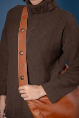 Bolso tipo bandolera de gamuza color marrón, con correa ancha ajustable decorada con tachas metálicas y cierre superior.