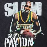 Remera de algodón color negro con efecto lavado, de corte holgado y manga corta. Presenta un estampado gráfico frontal estilo vintage con la imagen del jugador de básquetbol Gary Payton con la camiseta de los Seattle SuperSonics, junto con el texto 'SLAM', 'GARY PAYTON' y 'A GLOVE SUPREME'. Incluye un parche decorativo en la parte inferior derecha con el logo de la marca Mitchell & Ness y el equipo.